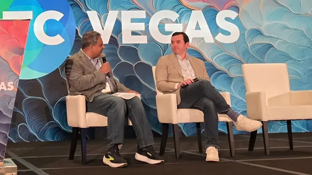 Two panelists seated on white chairs on the ITC Vegas stage, one speaking into a microphone.